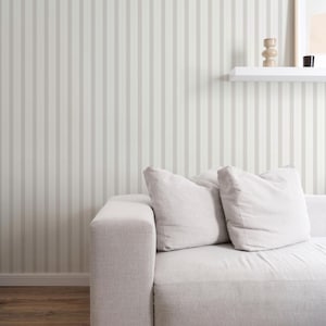 May include: A white sofa with two pillows sits in front of a wall with vertical stripes. The wall is painted in a light beige color with darker beige stripes.