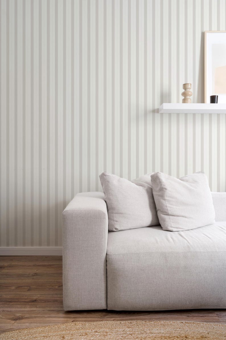 May include: A white sofa with two pillows sits in front of a wall with vertical stripes. The wall is painted in a light beige color with darker beige stripes.