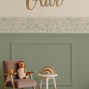 May include: A light green wall with a white border and a wooden name sign that says "Olive". The wall has a wallpaper border with a woodland animal design. A brown chair with a stuffed hedgehog sits next to a white stool with a rainbow wooden toy on top.