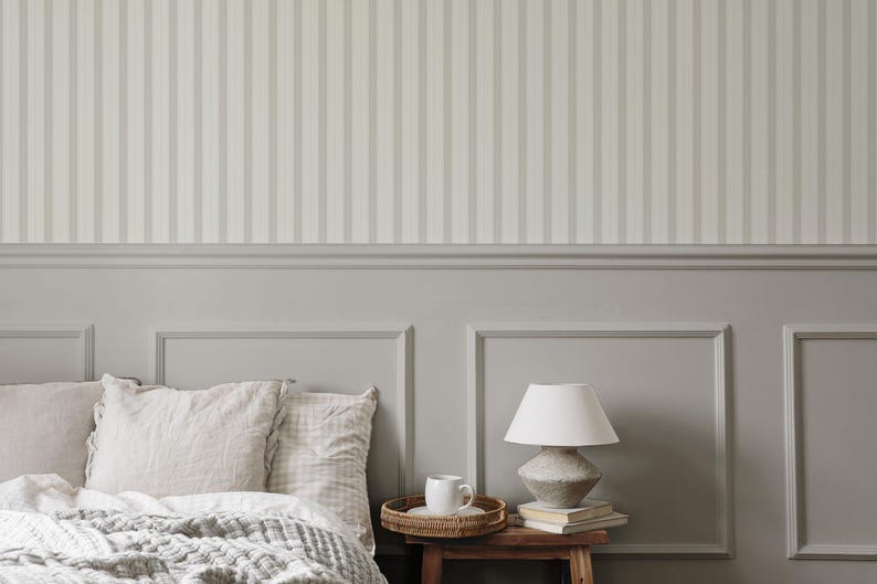 May include: A white bed with a gray and white striped headboard and a gray and white patterned blanket. There is a white ceramic mug on a wooden tray next to a lamp with a white shade on a wooden table.