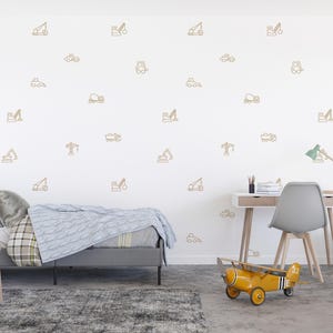 May include: A child's bedroom with a white wall decorated with gold-coloured construction vehicle decals. The room features a grey bed, a wooden desk, a grey chair, and a yellow toy aeroplane. The text "WEST COAST WALLS" is visible.