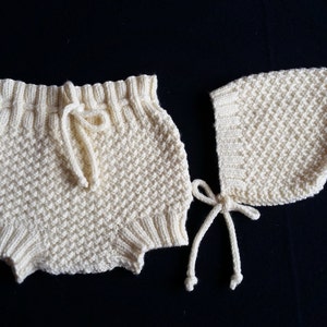 Può includere: Un set di vestiti per neonati in maglia di colore crema. Il set comprende un paio di pantaloncini con coulisse in vita e un berretto con un laccio.