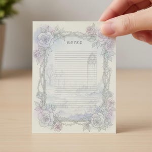May include: A rectangular note card held by a hand, featuring a floral border of roses and thorns. The card has a watercolor background with a gothic church illustration and the word "notes" at the top. Lined for writing.