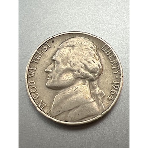 Op de afbeelding: Een zilveren Amerikaanse halve dollar munt met de inscriptie "IN GOD WE TRUST" en "LIBERTY 1964" op de voorzijde. De munt toont een profiel van Thomas Jefferson.