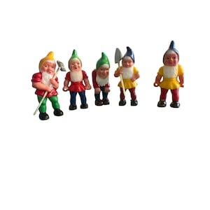 Peut inclure: Cinq petites figurines colorées de gnomes avec différents outils. Les gnomes portent des chapeaux rouges, jaunes et verts et ont des barbes blanches. Ils tiennent une râteau, une pelle et une pioche.