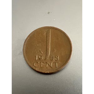 Puede incluir: Una moneda de un céntimo de cobre de los Países Bajos de 1958. La moneda presenta el número "1" en una fuente estilizada y la palabra "CENT" debajo.
