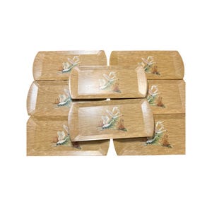 May include: A set of eight wooden trays with a woodgrain pattern and a painted design of white birds flying over a marsh. The trays are rectangular and have a slightly raised edge.