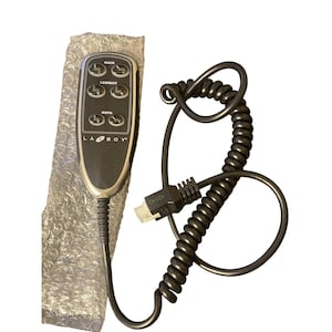 May include: A black and silver La-Z-Boy recliner remote control with buttons for back and leg rest adjustments. The remote has a coiled cord and a connector.