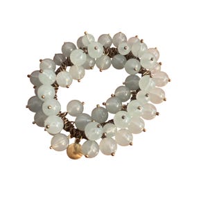 Op de afbeelding: Een armband met lichtgroene en witte kralen, gegroepeerd. De kralen zijn geregen op een goudkleurige ketting, met een kleine gouden bedel. De armband is ontworpen om om de pols te worden gedragen.