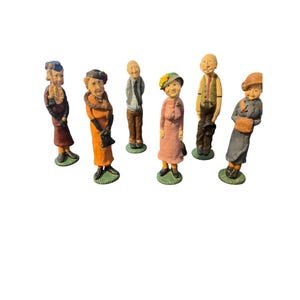 May include: A collection of seven small, hand-painted figurines depicting elderly people in various outfits. The figurines are on green circular bases and feature detailed clothing and facial expressions. The color palette includes shades of orange, pink, blue, and brown.