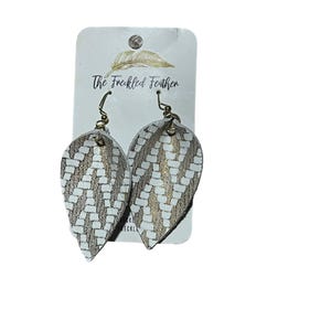 May include: A pair of leaf-shaped earrings with a white and gold woven pattern. The earrings hang from gold-coloured hooks and are displayed on a white card with the text "The Freckled Feather".
