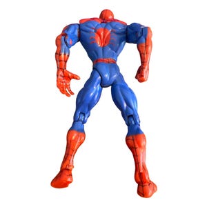 May include: A red and blue plastic action figure of Spider-Man. The figure is posed with its arms raised and its legs spread apart. The figure has a detailed design with a web pattern on its suit.