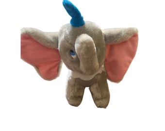 May include: A gray plush toy elephant with pink ears and a blue hat. The elephant has a sad expression on its face.