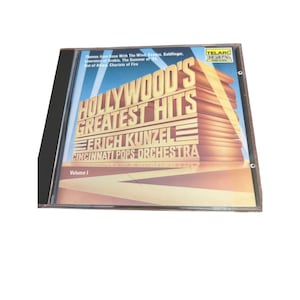 May include: A CD case with a gold and red design featuring the text "Hollywood's Greatest Hits" with the name "Erich Kunzel" and "Cincinnati Pops Orchestra" below. The text "Volume I" is in the bottom left corner.