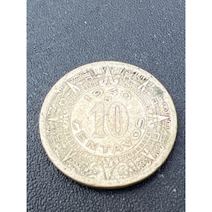 May include: Silver Mexican coin featuring a sun design with rays and the inscription "10 Centavos" around the edge.