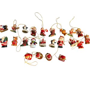 May include: A collection of Christmas ornaments in various shapes and designs. The ornaments include Santa Claus, snowmen, penguins, teddy bears, and other festive figures. Each ornament is detailed with bright colors and attached with a gold string for hanging.
