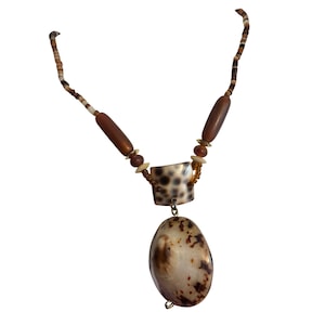 May include: A handcrafted necklace featuring a large, oval pendant with brown and cream tones. The necklace includes a square bead with a spotted pattern, wooden beads, and small, round beads in shades of brown and cream.