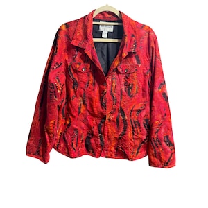 May include: A long-sleeved button-down jacket in vibrant red, orange, and black abstract patterns. The garment features a collared neckline, two chest pockets with button closures, and a black interior lining with a Chico's brand label.