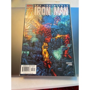 May include: Comic book cover featuring Iron Man in a red and gold suit, surrounded by a futuristic cityscape. The title "The Invincible Iron Man" is printed in bold letters at the top of the cover. The cover also includes the names "Busiek" and "Chen" in the bottom right corner.