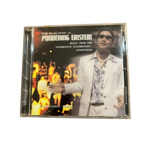 Könnte beinhalten: Eine CD-Hülle mit dem Album "Pondering Einstein" und dem Text "Music from the Sockmuffin Documentary Soundtrack". Das Cover zeigt einen Mann in weißem Anzug und Sonnenbrille. Die Worte "Promotional Album" sind ebenfalls sichtbar.