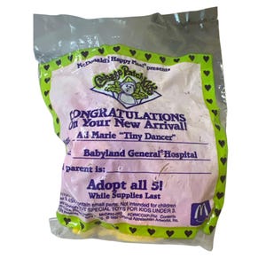 Puede incluir: Un empaque de juguete Happy Meal Cabbage Patch Kids rosa y blanco con un borde verde y corazones. El empaque presenta el logotipo de Cabbage Patch Kids y el texto "¡Felicidades por tu nueva llegada!"  "Ad Marie "Tiny Dancer" Babyland General Hospital" y "¡Adopta los 5! Mientras duren las existencias".
