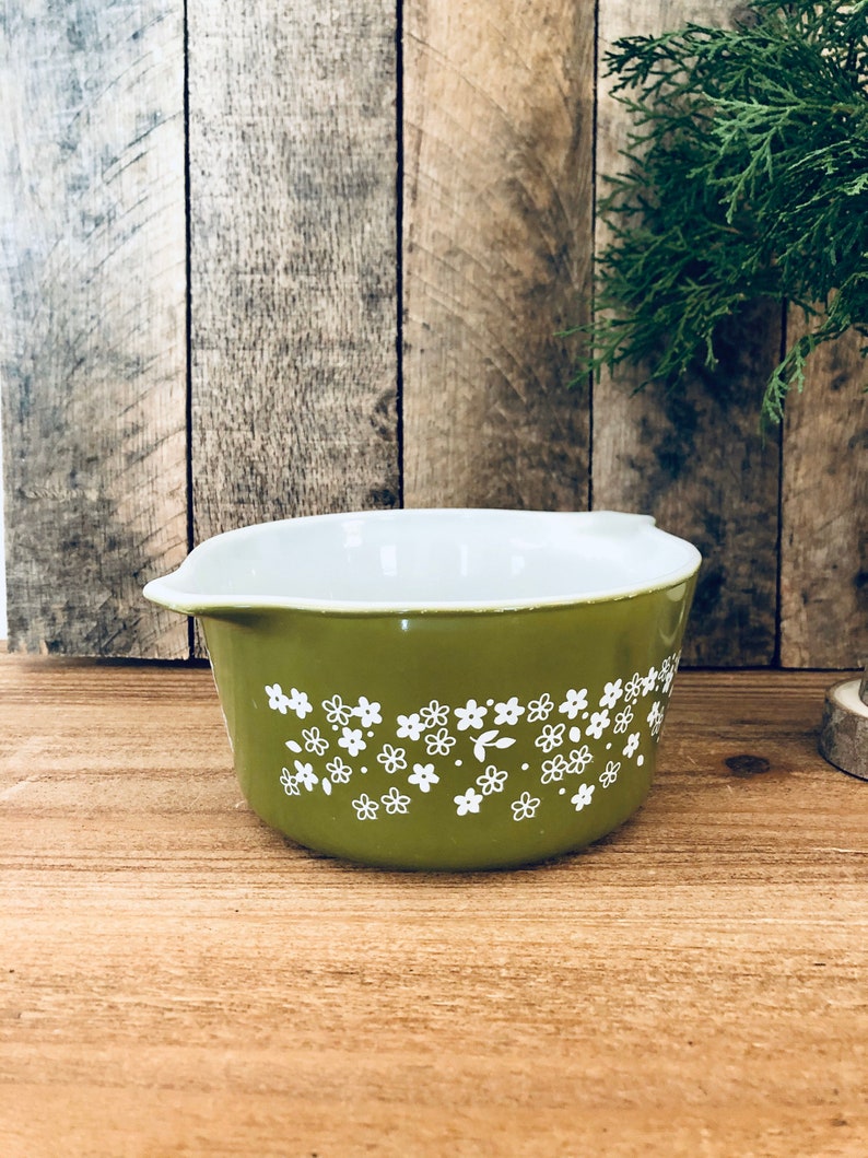 May include: A green casserole dish with a white floral pattern. The dish has a white interior and a rounded shape.
