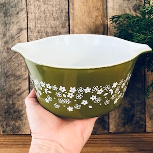 May include: A green ceramic mixing bowl with a white floral pattern. The bowl has two handles on the sides.