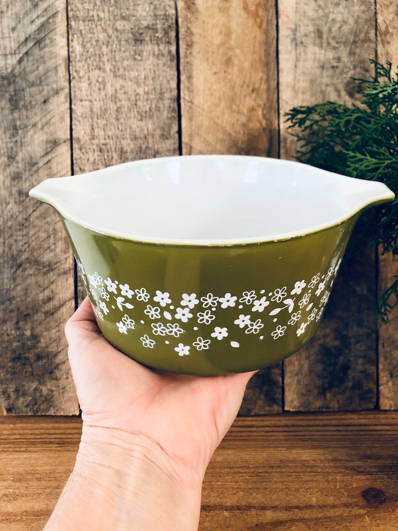 May include: A green ceramic mixing bowl with a white floral pattern. The bowl has two handles on the sides.
