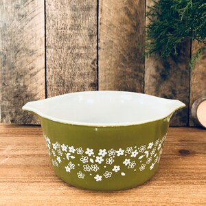 May include: A green ceramic baking dish with a white floral pattern. The dish has two handles on the sides.