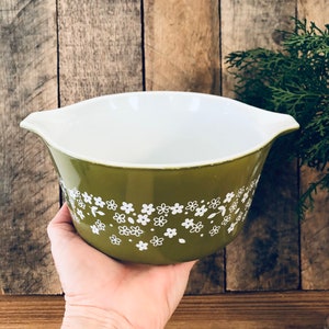 May include: A green ceramic mixing bowl with a white floral pattern. The bowl has two handles on the sides.