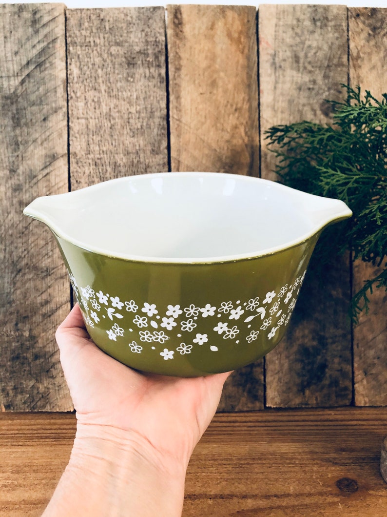 May include: A green ceramic mixing bowl with a white floral pattern. The bowl has two handles on the sides.