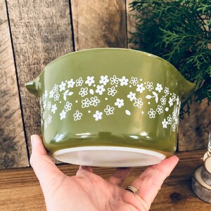 May include: A green ceramic baking dish with a white floral pattern. The dish has a rounded shape and a handle on one side.