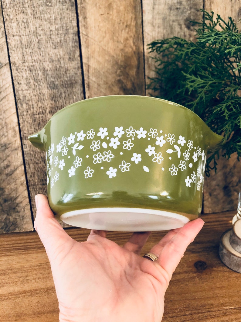 May include: A green ceramic baking dish with a white floral pattern. The dish has a rounded shape and a handle on one side.