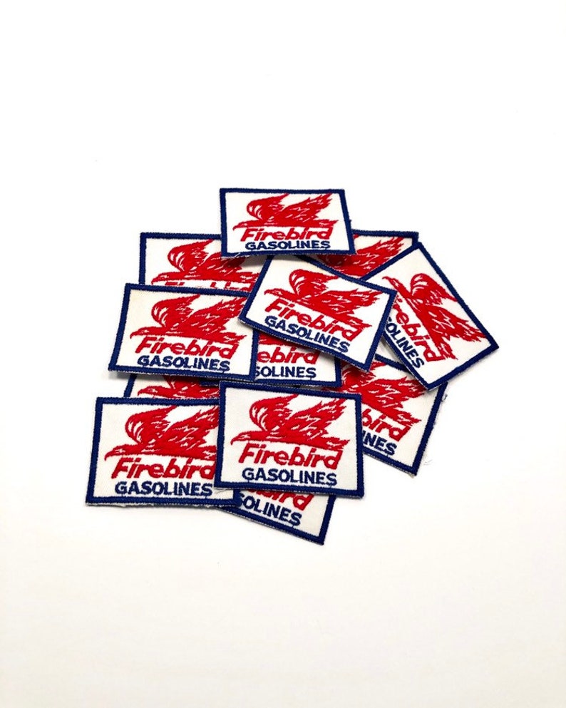 May include: A pile of vintage Firebird Gasolines patches. The patches are white with a red bird design and blue trim. The text "Firebird Gasolines" is printed in blue on each patch.