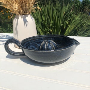 Może przedstawiać: Ceramiczny wyciskacz do cytrusów w ciemnoniebieskim kolorze z uchwytem i żebrowanym wyciskaczem w środku. Wyciskacz stoi na białej powierzchni.