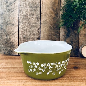 May include: A green ceramic baking dish with a white floral pattern. The dish has a rounded shape and a white interior.