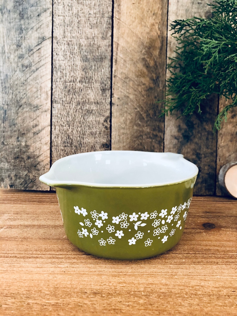 May include: A green ceramic baking dish with a white floral pattern. The dish has a rounded shape and a white interior.