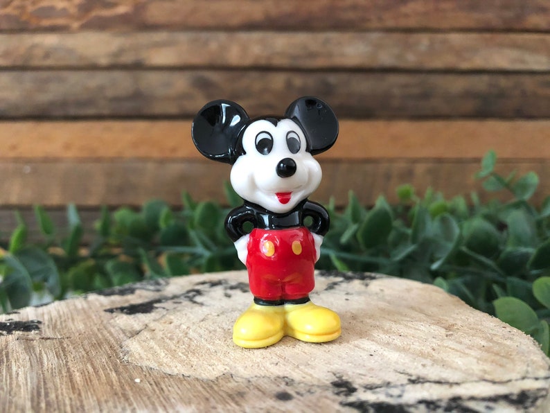 May include: A small, black and white ceramic figurine of Mickey Mouse. He is wearing red shorts with a yellow button and yellow shoes. He is standing with his hands on his hips.