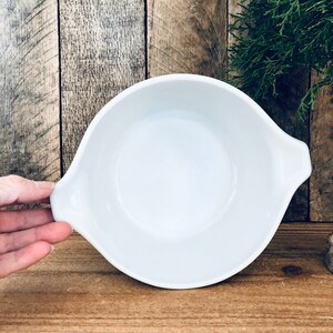 May include: White ceramic baking dish with two handles. The dish is empty and has a slight green tint around the rim.