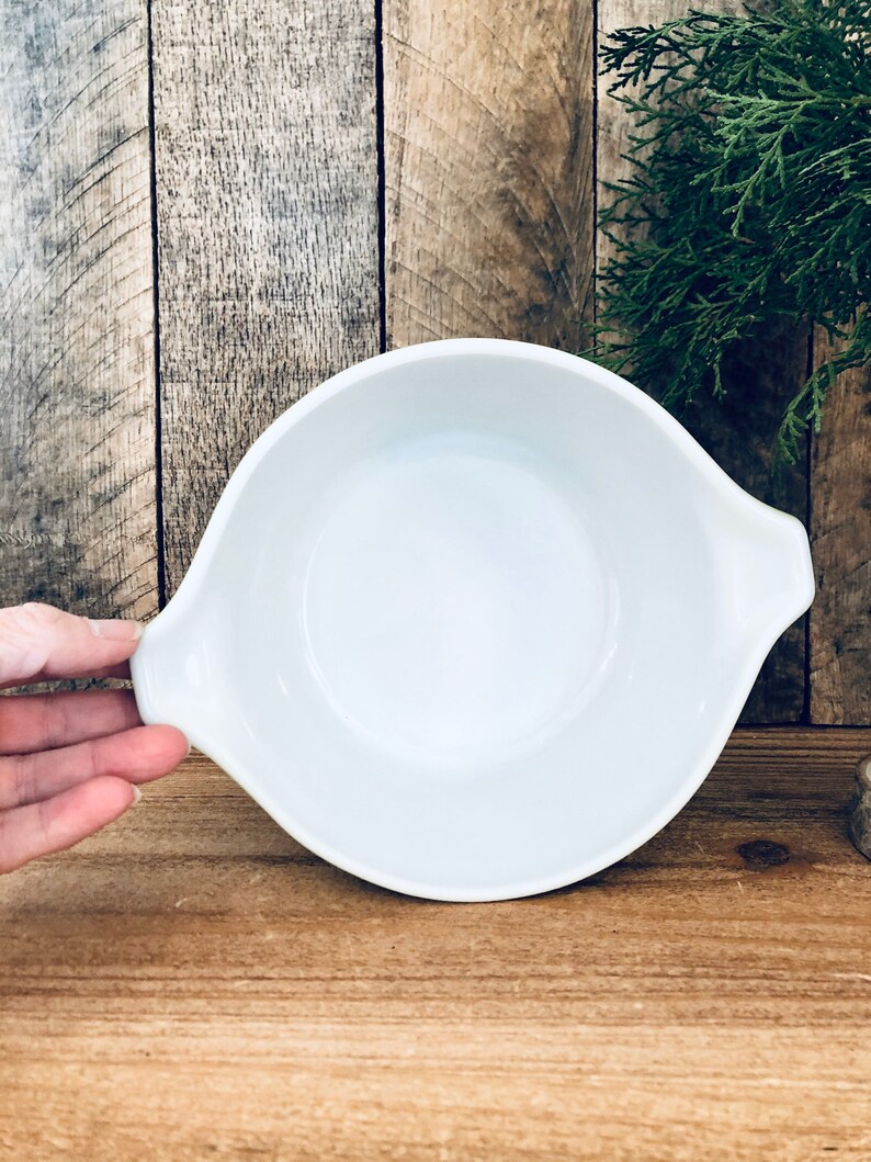 May include: White ceramic baking dish with two handles. The dish is empty and has a slight green tint around the rim.