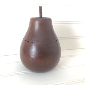 May include: A dark brown wooden pear-shaped box with a lid. The box is made of wood and has a smooth finish.