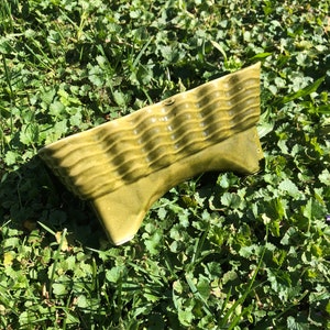 May include: A green ceramic planter with a wavy design. The planter is sitting on a bed of green grass.