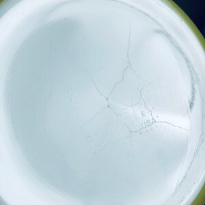 May include: The bottom of a white ceramic bowl with a green rim. The bowl has a crack running through the center. The text "O.H.  COATING  U.S.A." is visible on the bottom of the bowl.