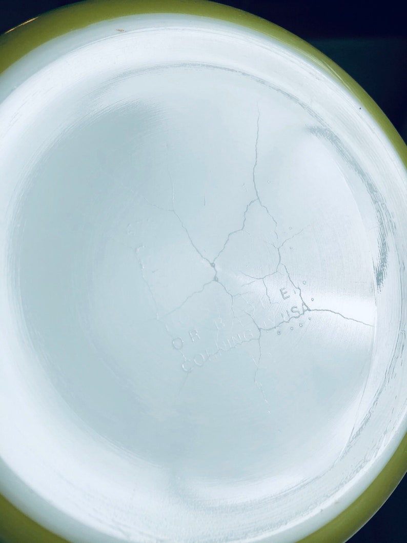 May include: The bottom of a white ceramic bowl with a green rim. The bowl has a crack running through the center. The text "O.H.  COATING  U.S.A." is visible on the bottom of the bowl.