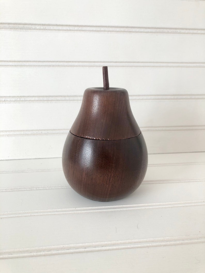 May include: A dark brown wooden pear-shaped box with a lid. The box is made of wood and has a smooth finish.
