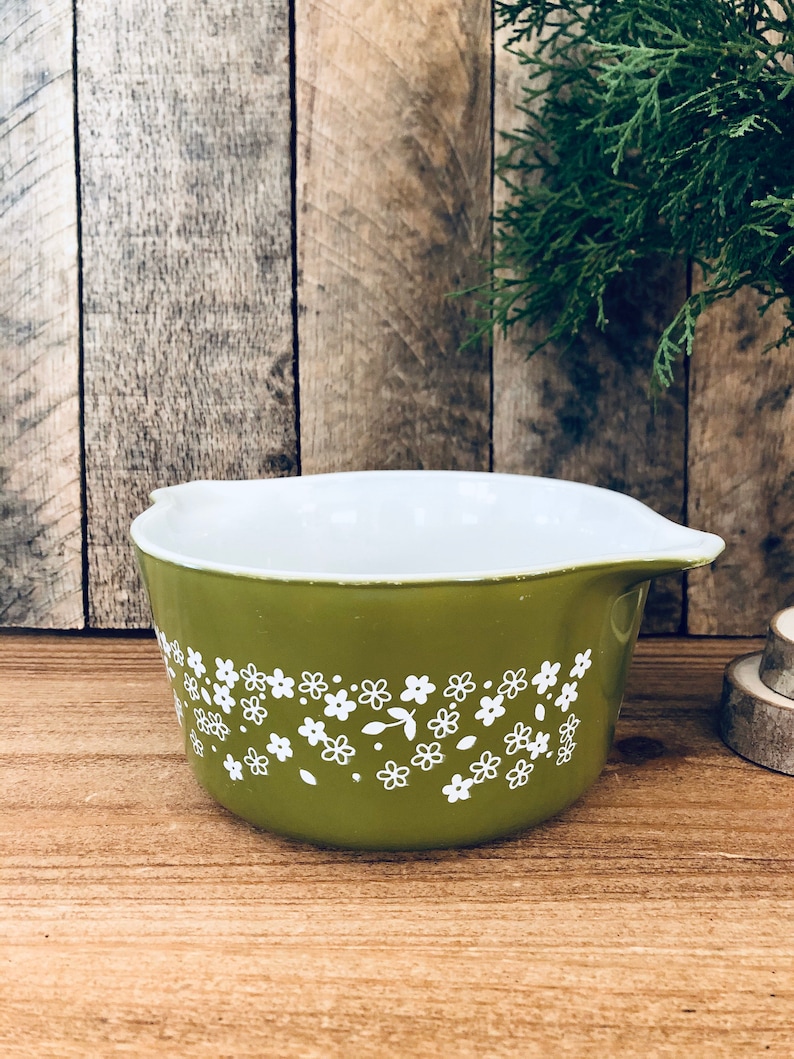 May include: A green ceramic baking dish with a white floral pattern. The dish has a rounded shape and a pouring spout.