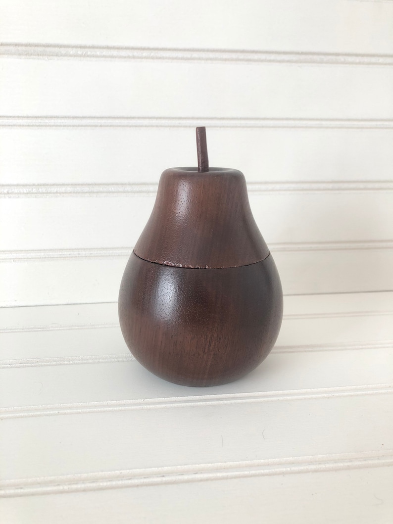 May include: A dark brown wooden pear-shaped box with a lid. The box is made of wood and has a smooth finish.