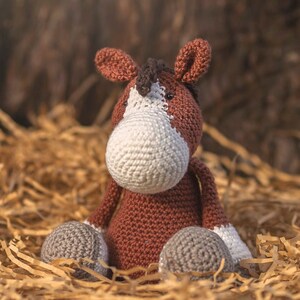 Puede incluir: Un juguete de caballo de crochet marrón y blanco sentado en una cama de papel triturado.