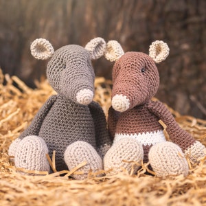 May include: Two crocheted stuffed mice, one gray and one brown, sitting in a nest of shredded paper. The mice have white noses and feet.