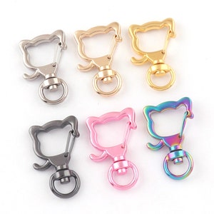 May include: Six different colored metal cat-shaped keychains with a swivel clasp. The keychains are silver, gold, pink, black, rainbow, and a darker silver.
